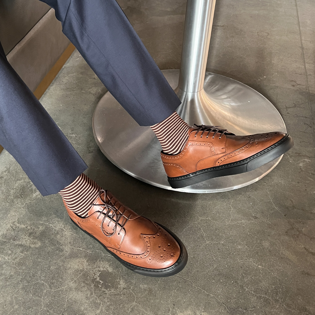 Cognac wingtip oxford shoes with striped socks and black rubber sole