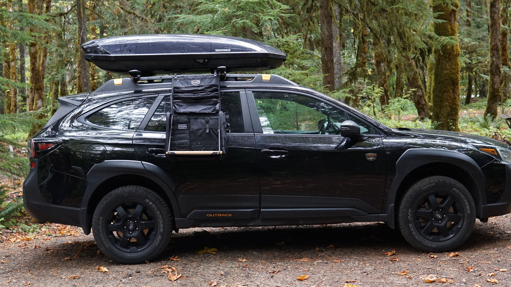 Black mobile camp kitchen bag mounted on an SUV roof rack, secured with straps