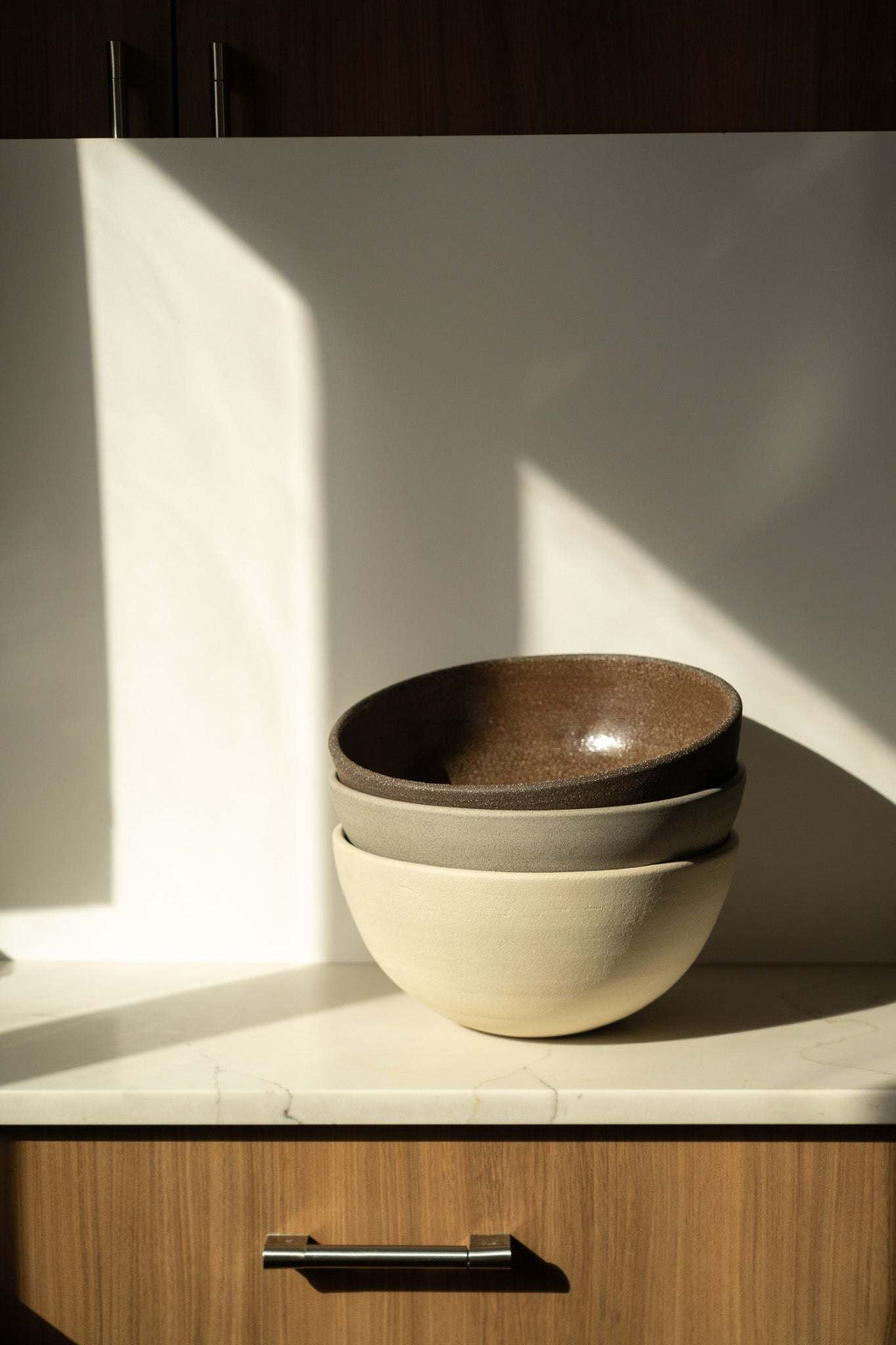 Stoneware fruit bowl set display: dark bowl nested in light beige bowl.
