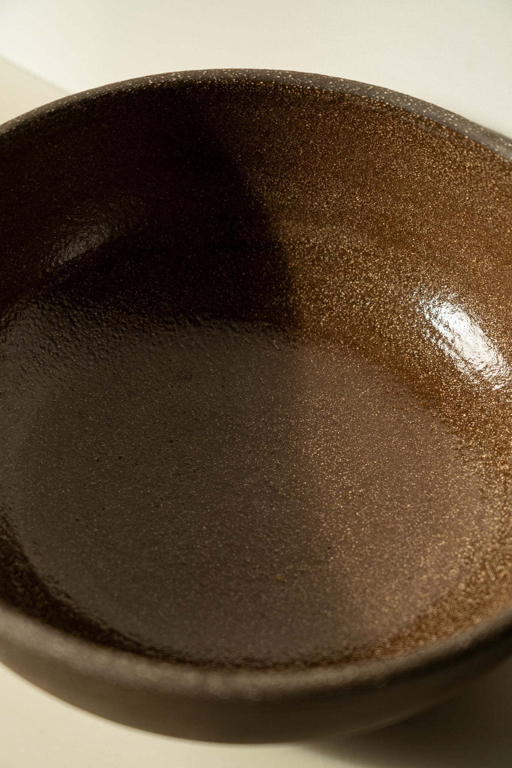 Stoneware fruit bowl interior, dark brown speckled glaze with glossy sheen.
