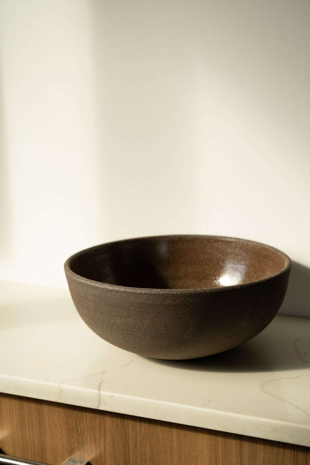 Stoneware fruit bowl, dark brown with speckled glaze, wide round shape.