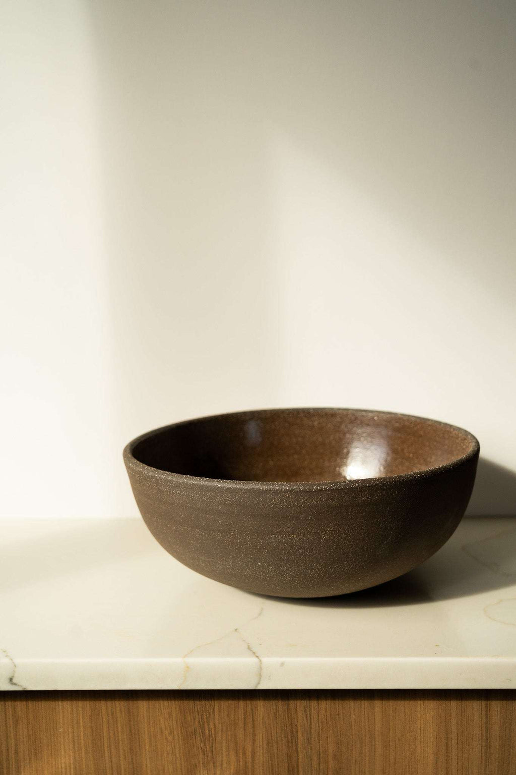 Stoneware fruit bowl, dark brown speckled glaze on a wide round form.
