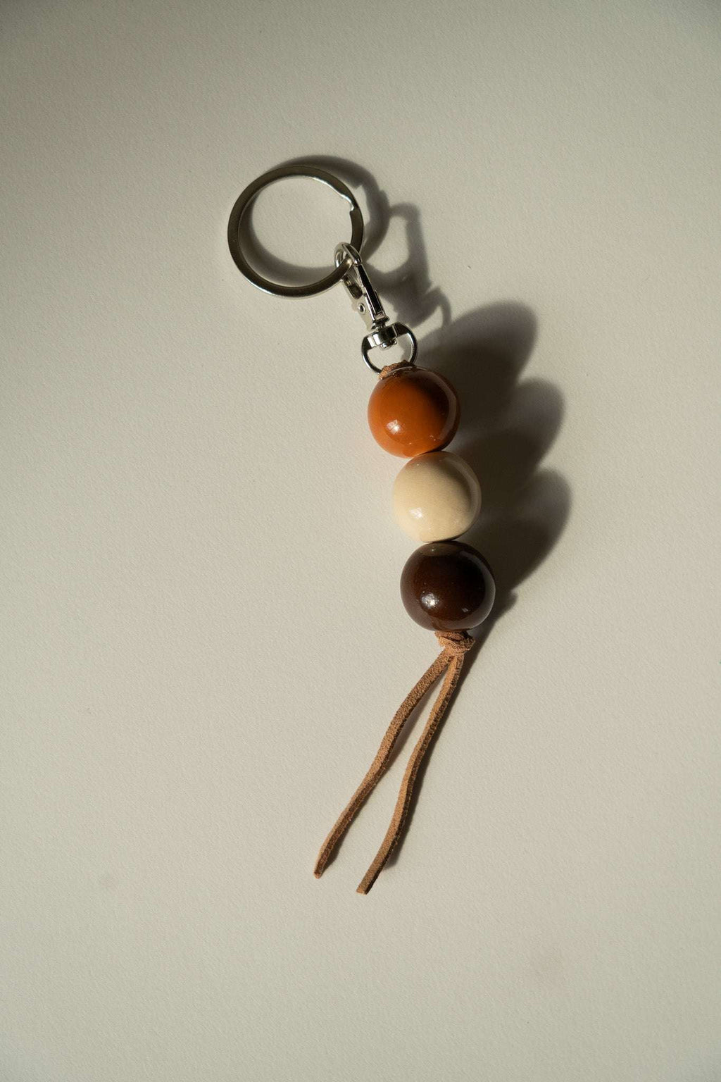 Handmade ceramic keychain with dark brown, cream, and orange beads and braided tassel