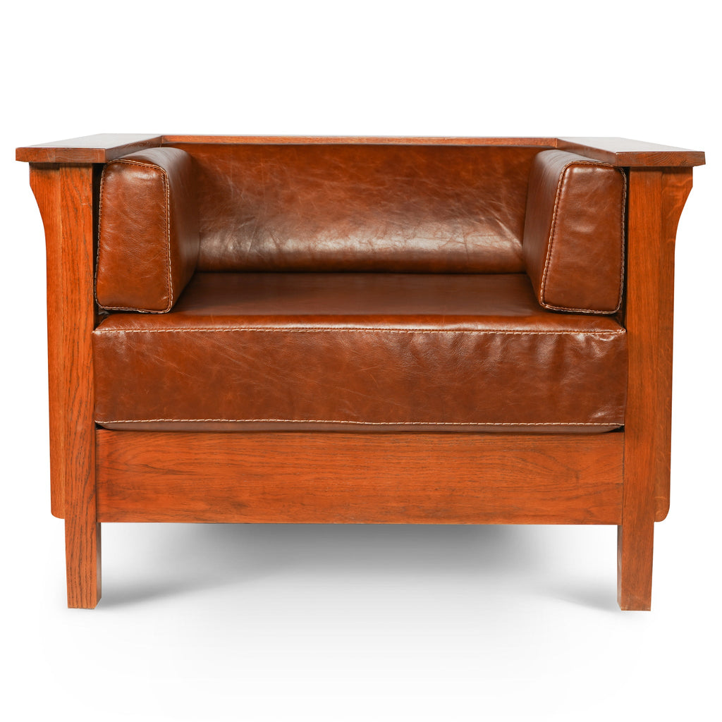 Brown leather side arm chair with two seat cushions, square arm pads, and wood legs.