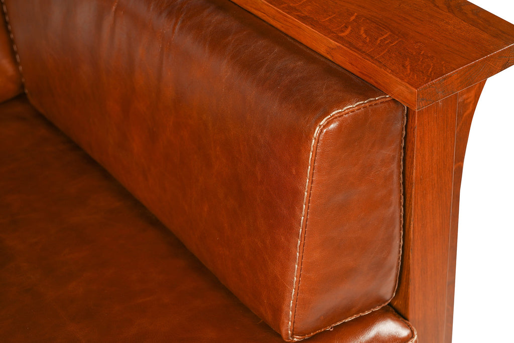 Brown leather chair arm corner with visible stitching on the padded armrest.