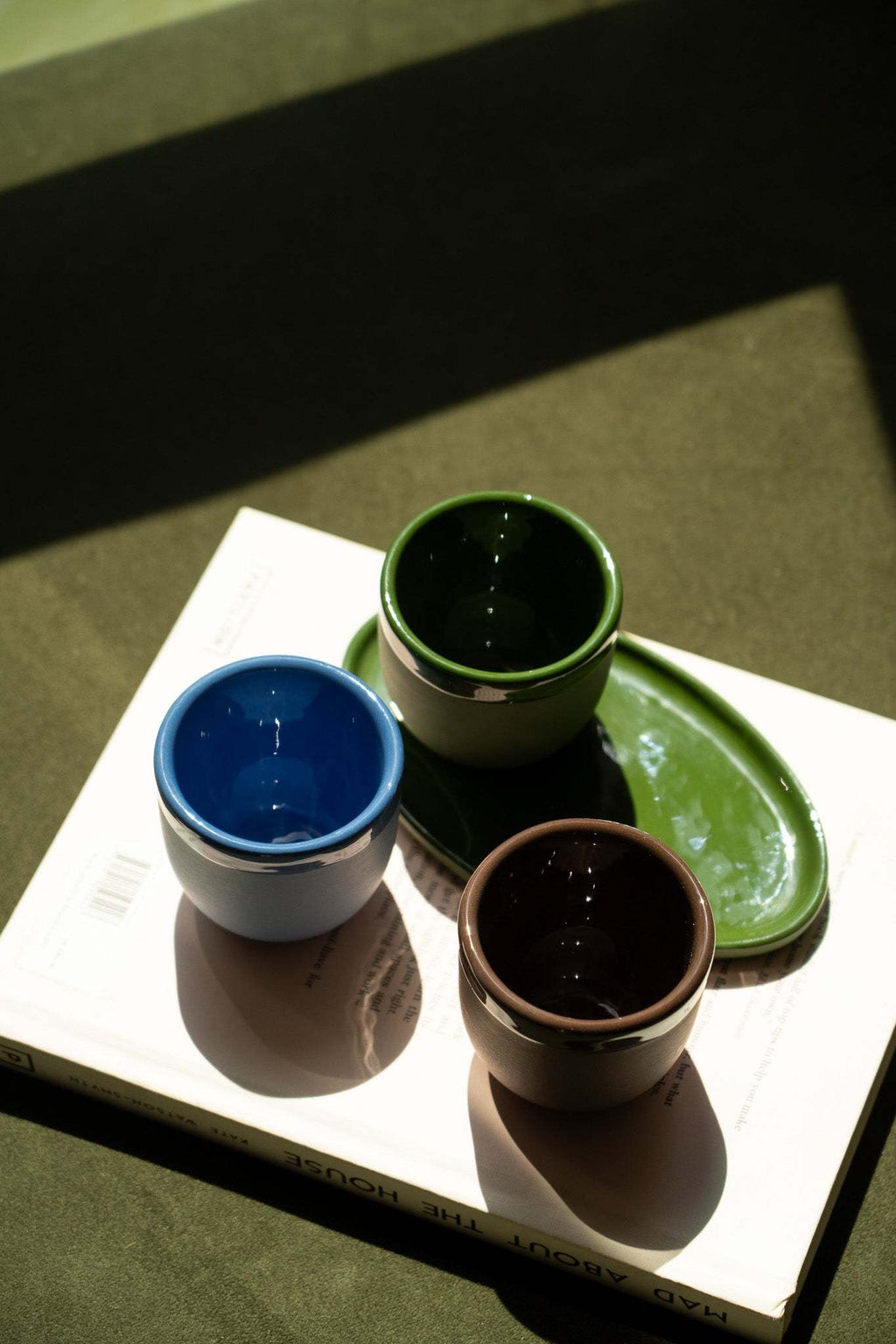 Ceramic espresso cups in blue, green, and brown arranged on a book.