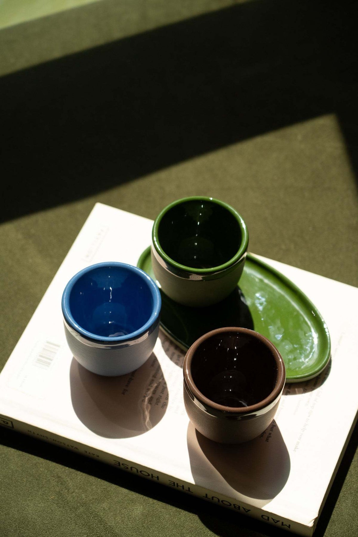 Ceramic espresso cups in blue, green, and brown arranged on a book.