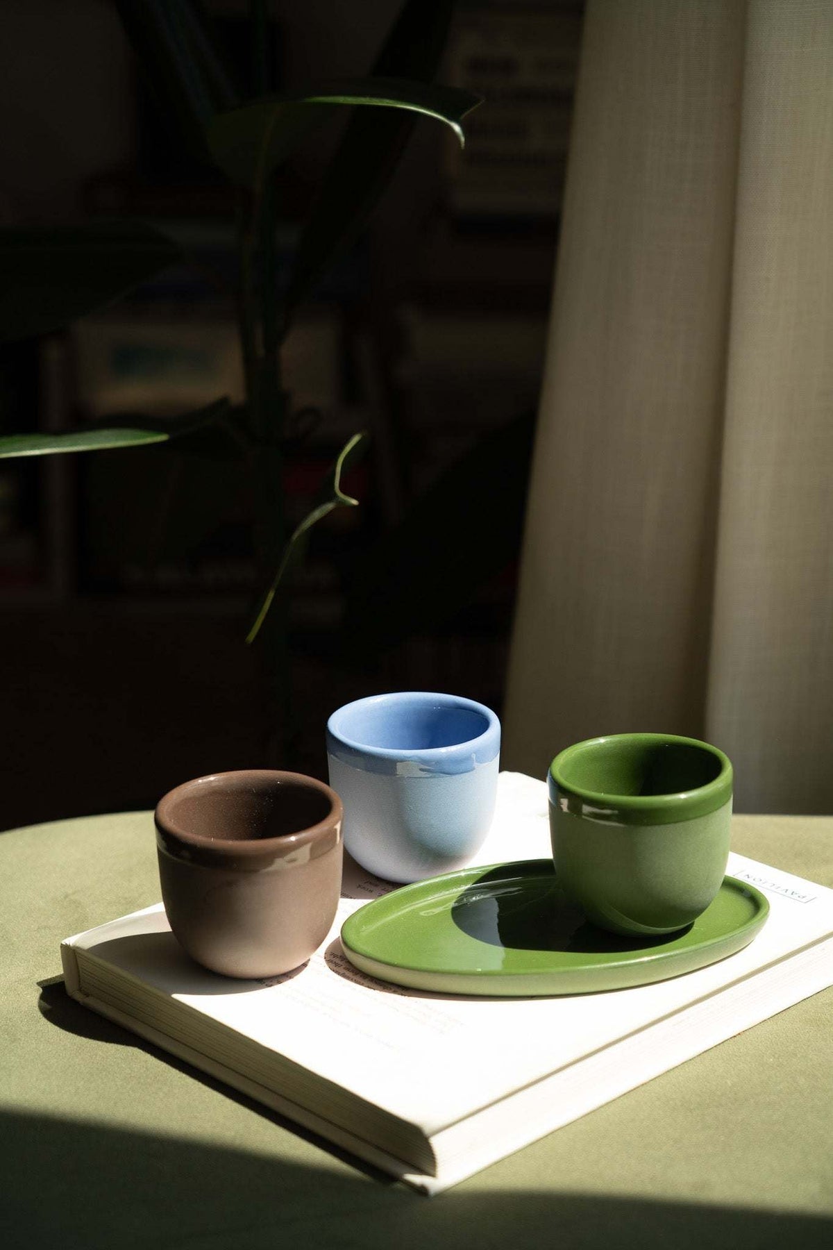 Three ceramic espresso cups with saucers: brown, blue, and green on an open book.