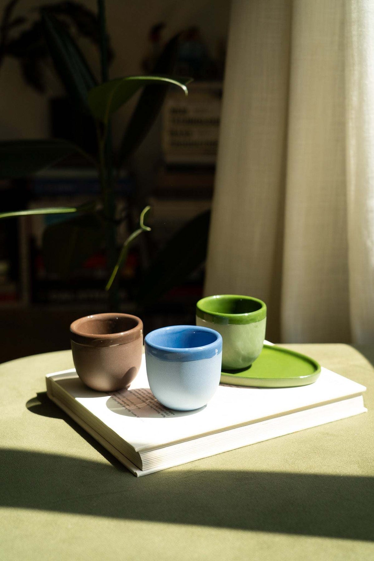 Ceramic espresso cup set on books: brown, blue, and green cups with saucers.