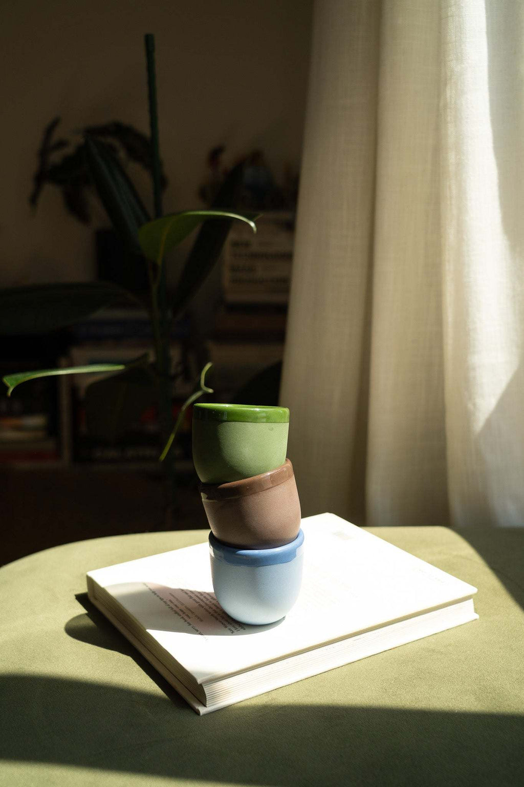 Stacked ceramic espresso cups in green and blue with matching saucers on a book.