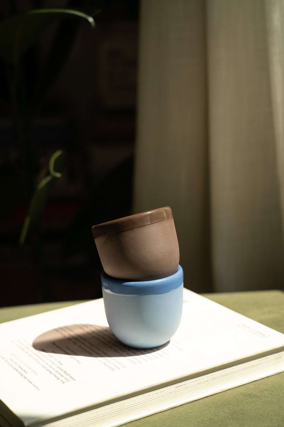 Blue ceramic espresso cup stacked on a light brown saucer, sunlit close-up.