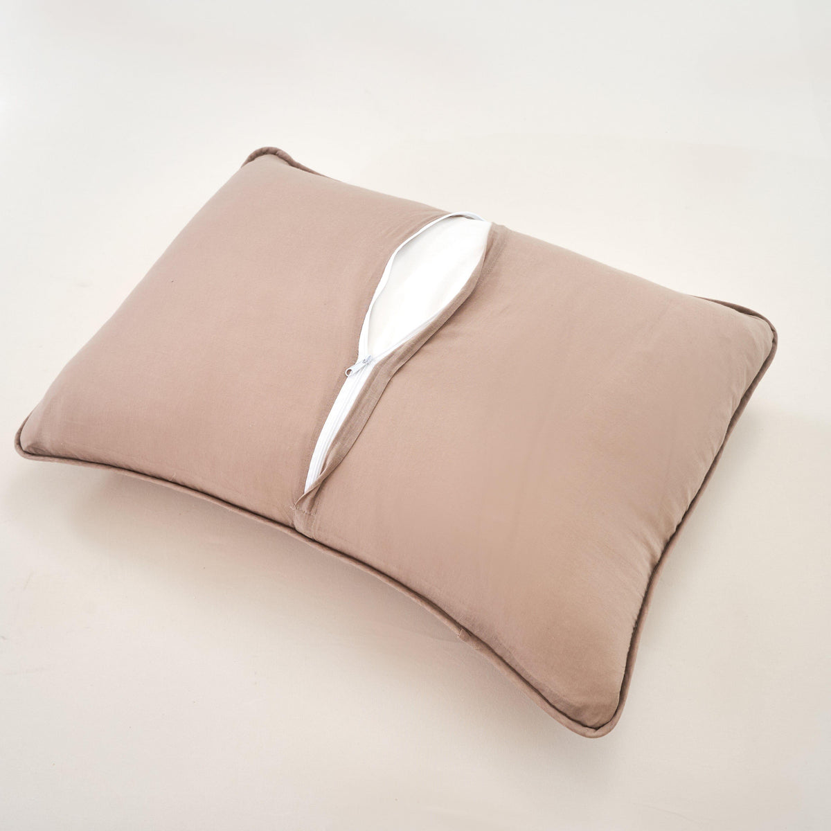 Taupe decorative pillow with white edge trim on matching quilted bedding