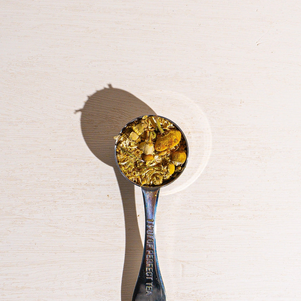 Spoon filled with golden chamomile tea leaves and petals