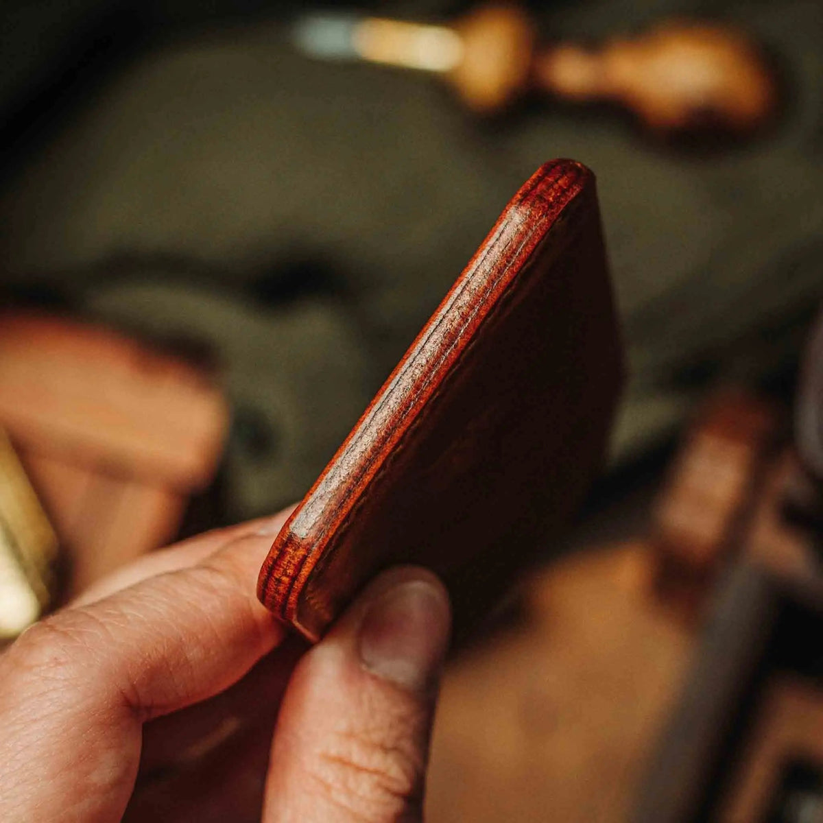 Slim leather wallet with dark red-brown edge, held in hand