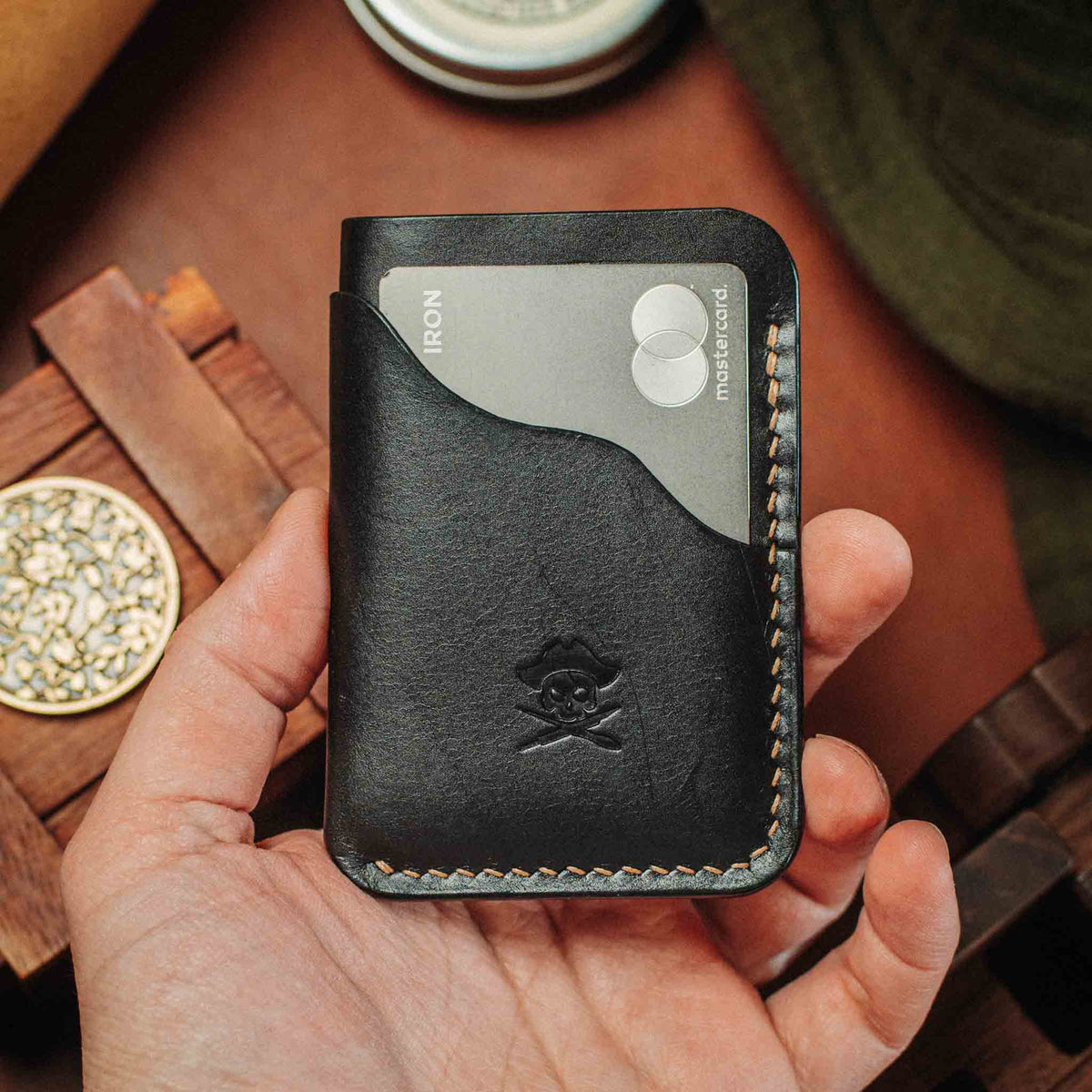 Black leather minimalist wallet held in hand with embossed skull emblem and edge stitching