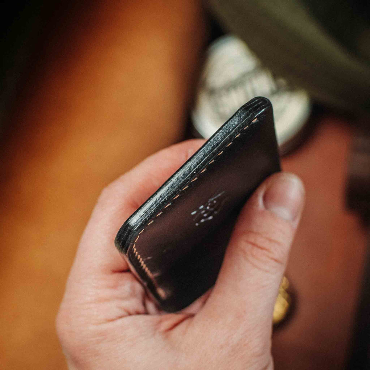 Black minimalist leather wallet in hand, side view showing slim profile and stitching