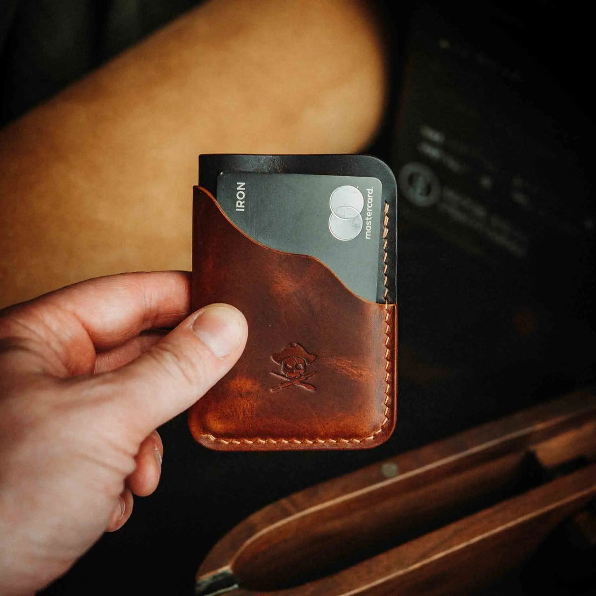 Brown minimalist leather wallet held in hand, front view with embossed logo and card slots