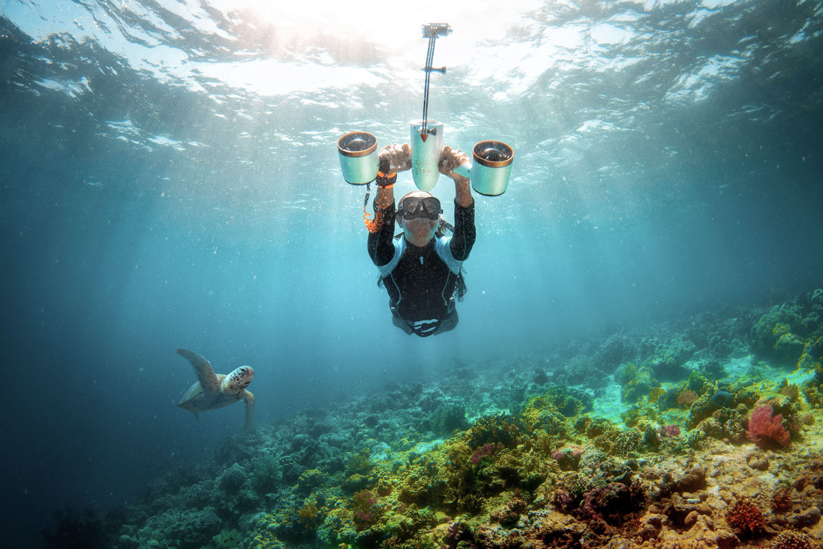 Underwater camera diver holding dual-lit camera rig with white-and-blue housing