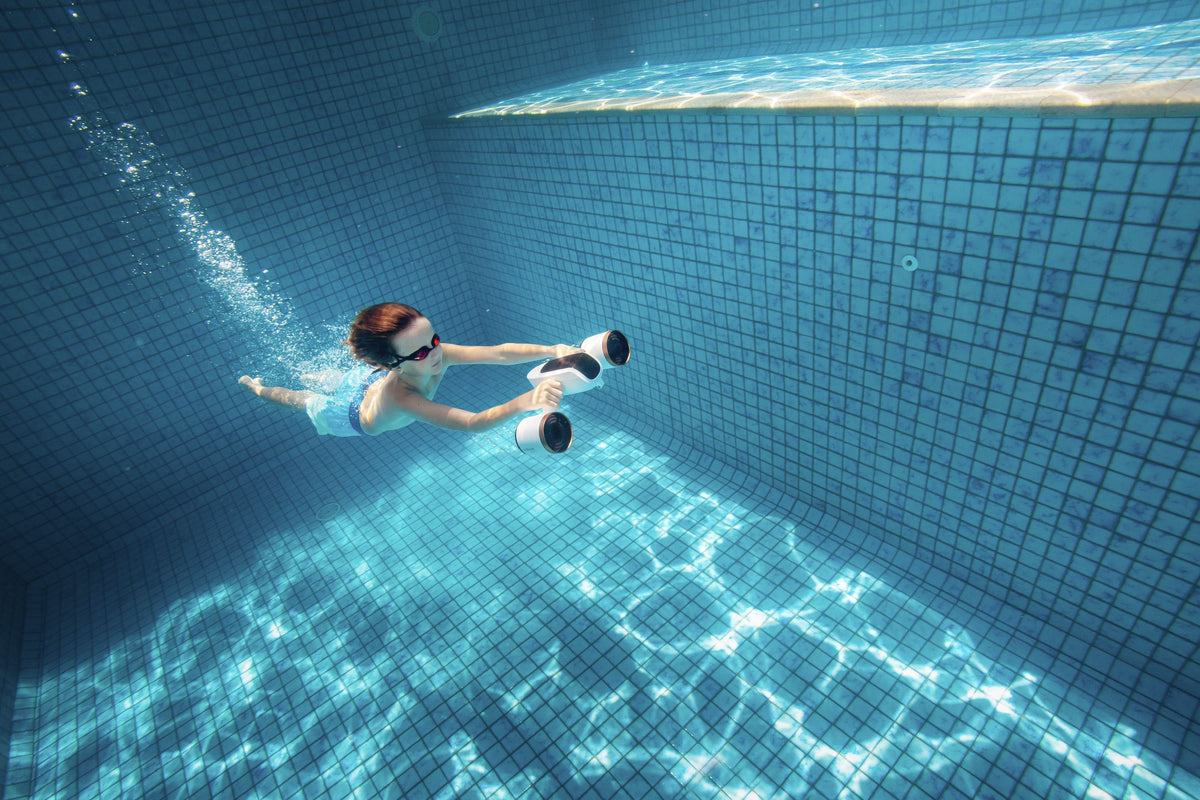 Underwater diver holding a white-and-black camera device while swimming