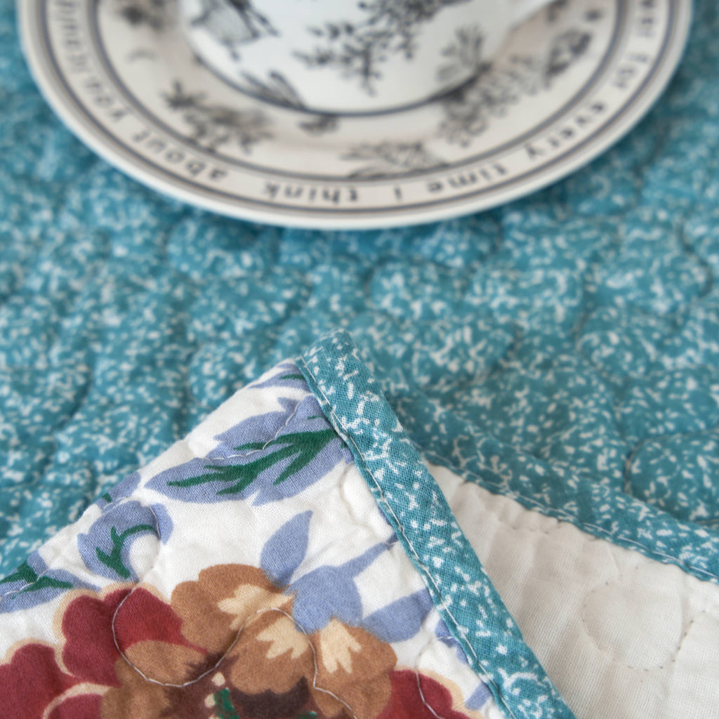 Quilted throw blanket corner detail; blue textured fabric edging with floral patch underneath