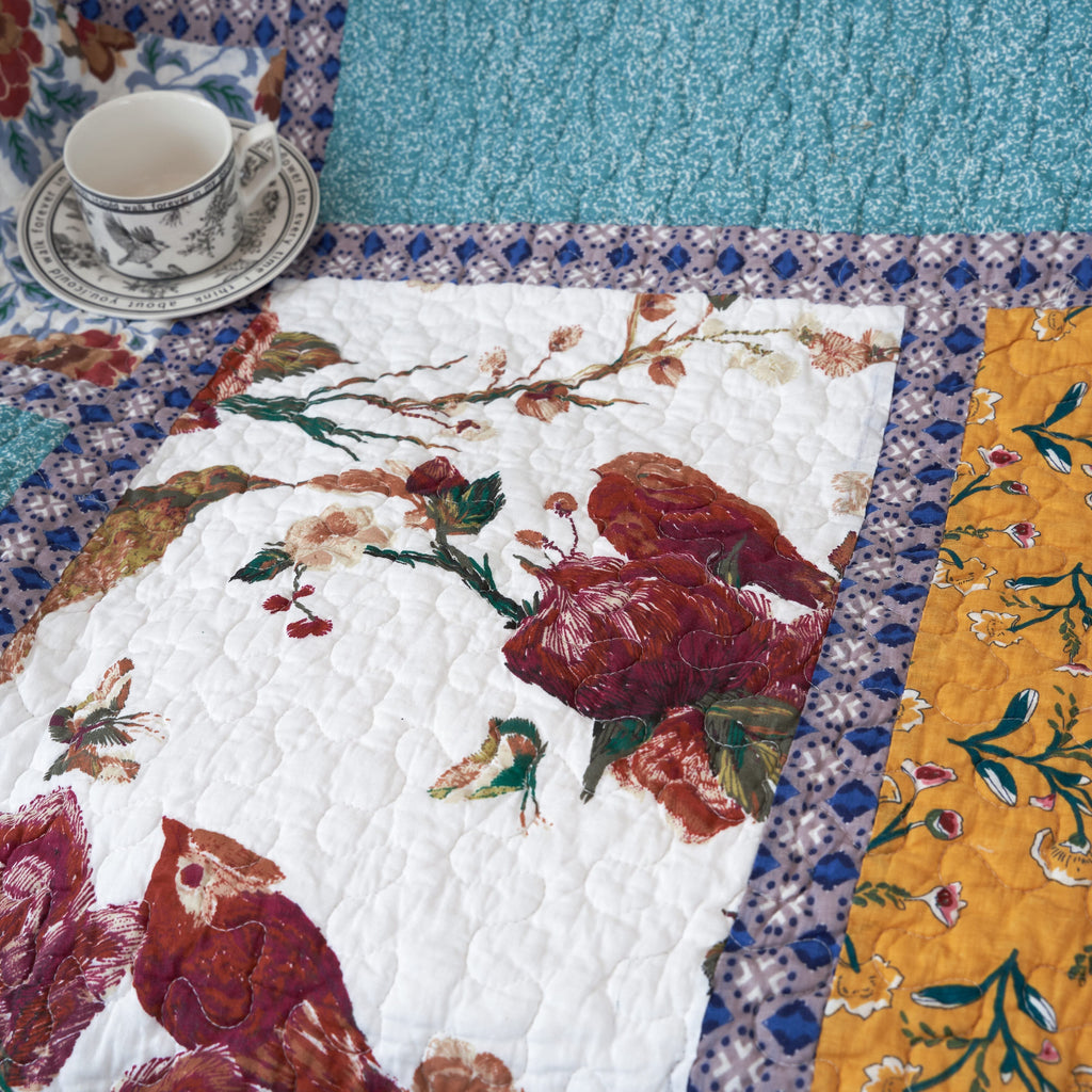 Quilted patchwork throw blanket top view with red rose and floral bird prints on white background