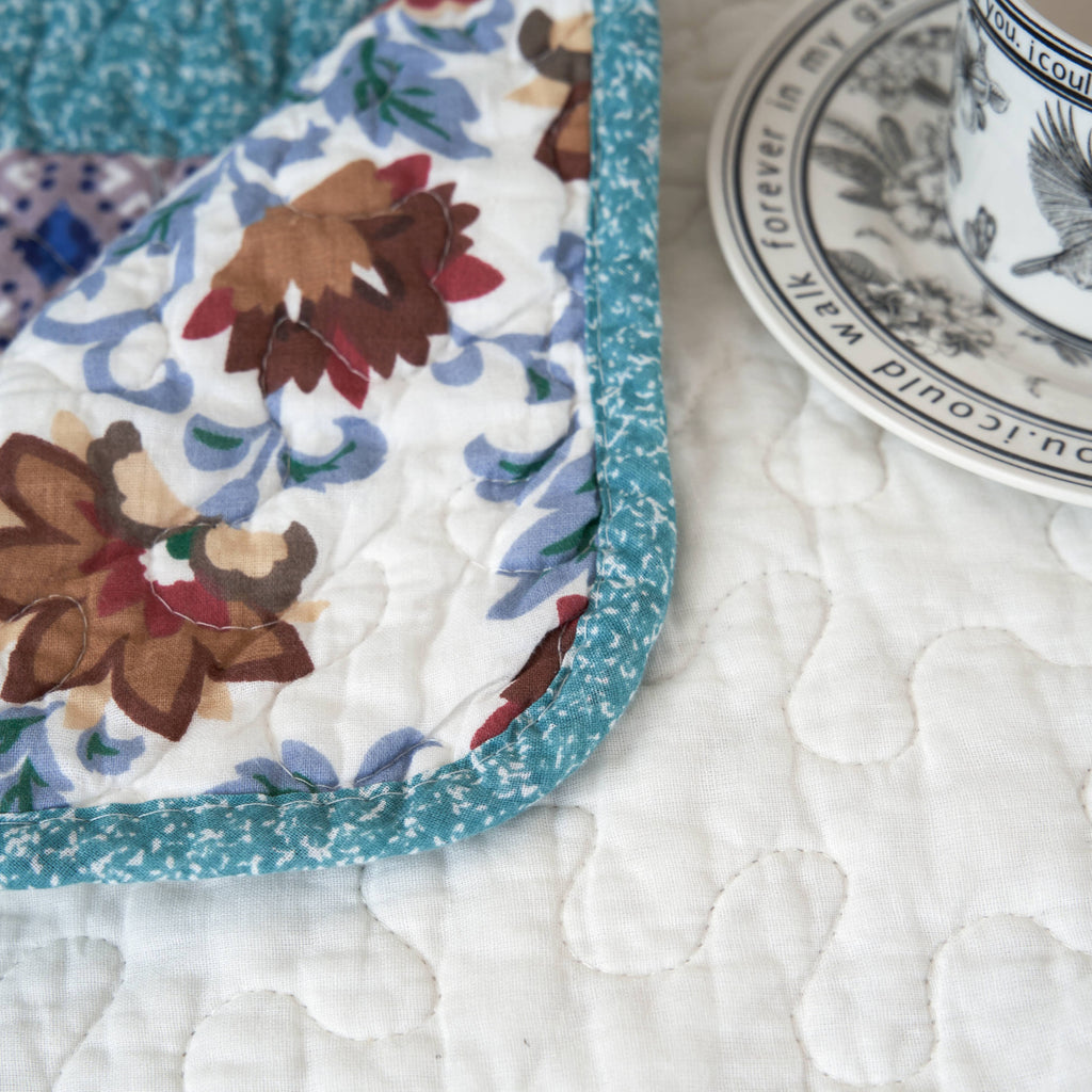 Quilted patchwork throw blanket corner close-up with white fabric and blue floral panel trim