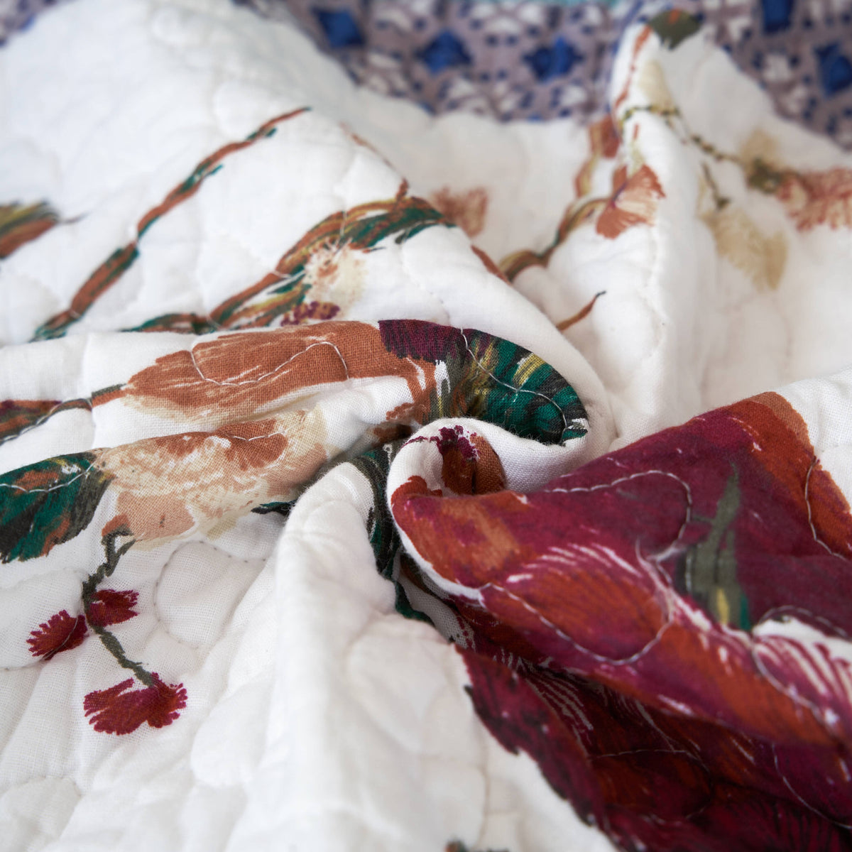Quilted throw blanket close-up showing white base with colorful floral and bird motifs