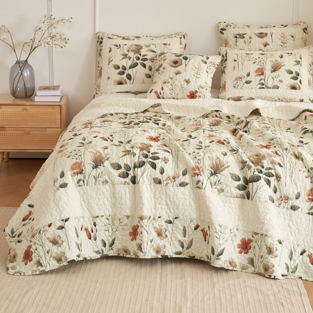 Floral quilt and matching throw pillows in off-white with beige, rose, and green botanical print.