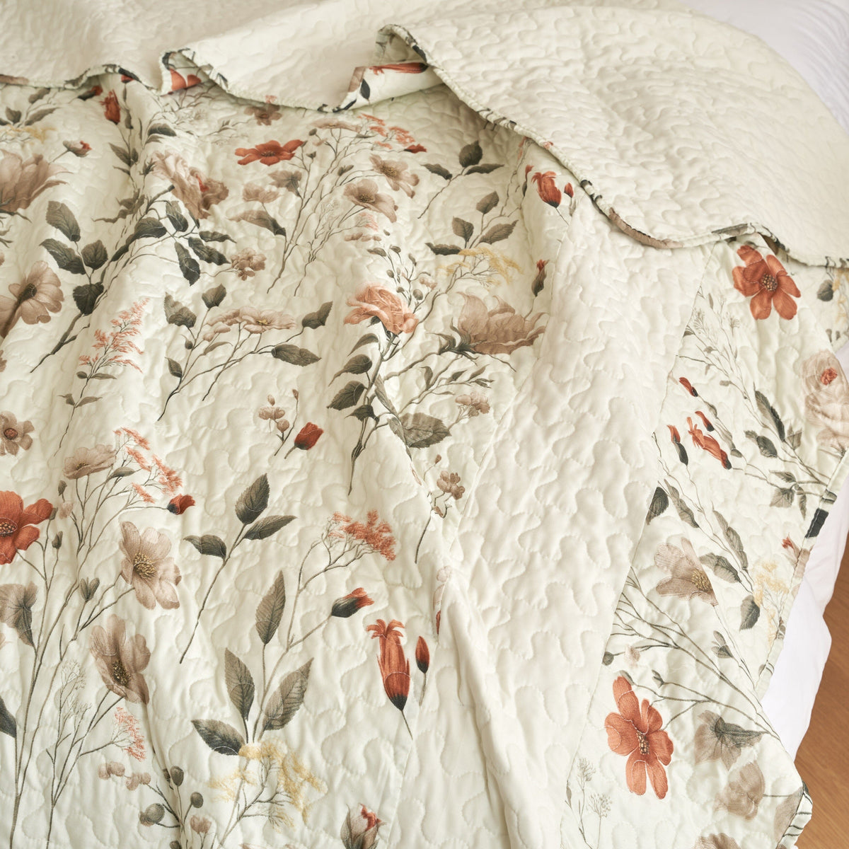 Close-up of cream floral quilt with green leaves and rust-orange flower details