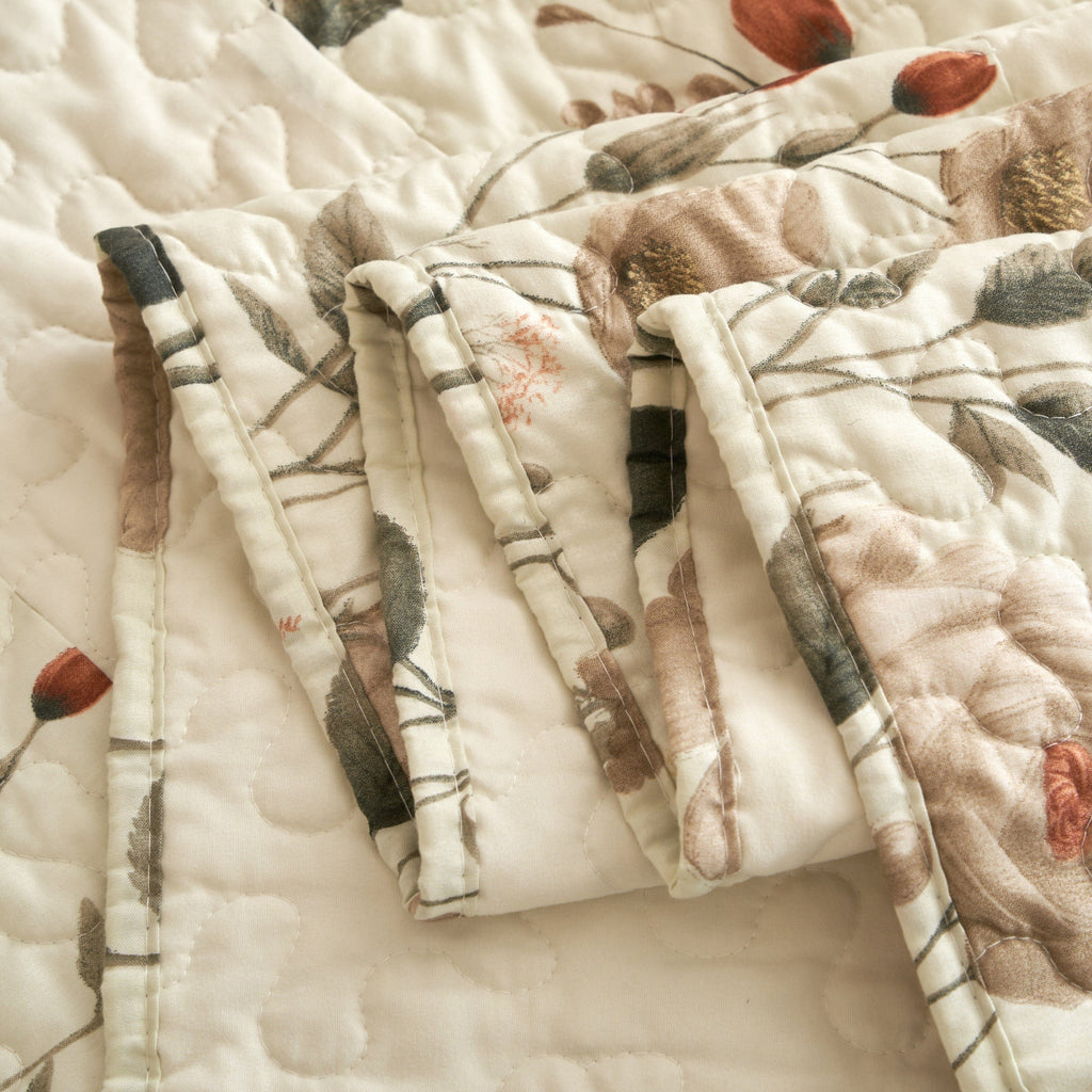 Close-up of quilted pillow shams with cream botanical print and stitched channels