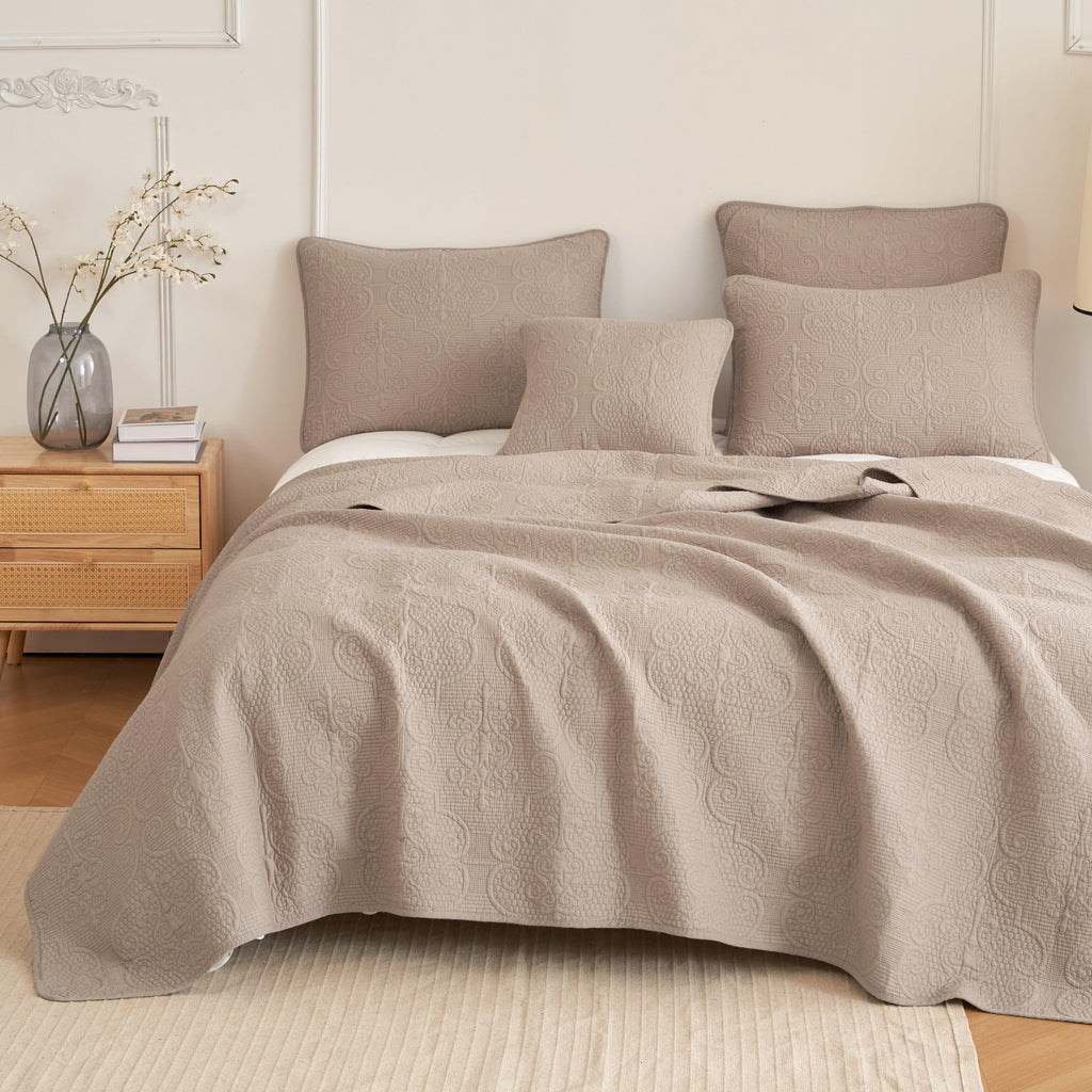 Quilted bedspread with swirled pattern in sandy taupe on a neatly made bed
