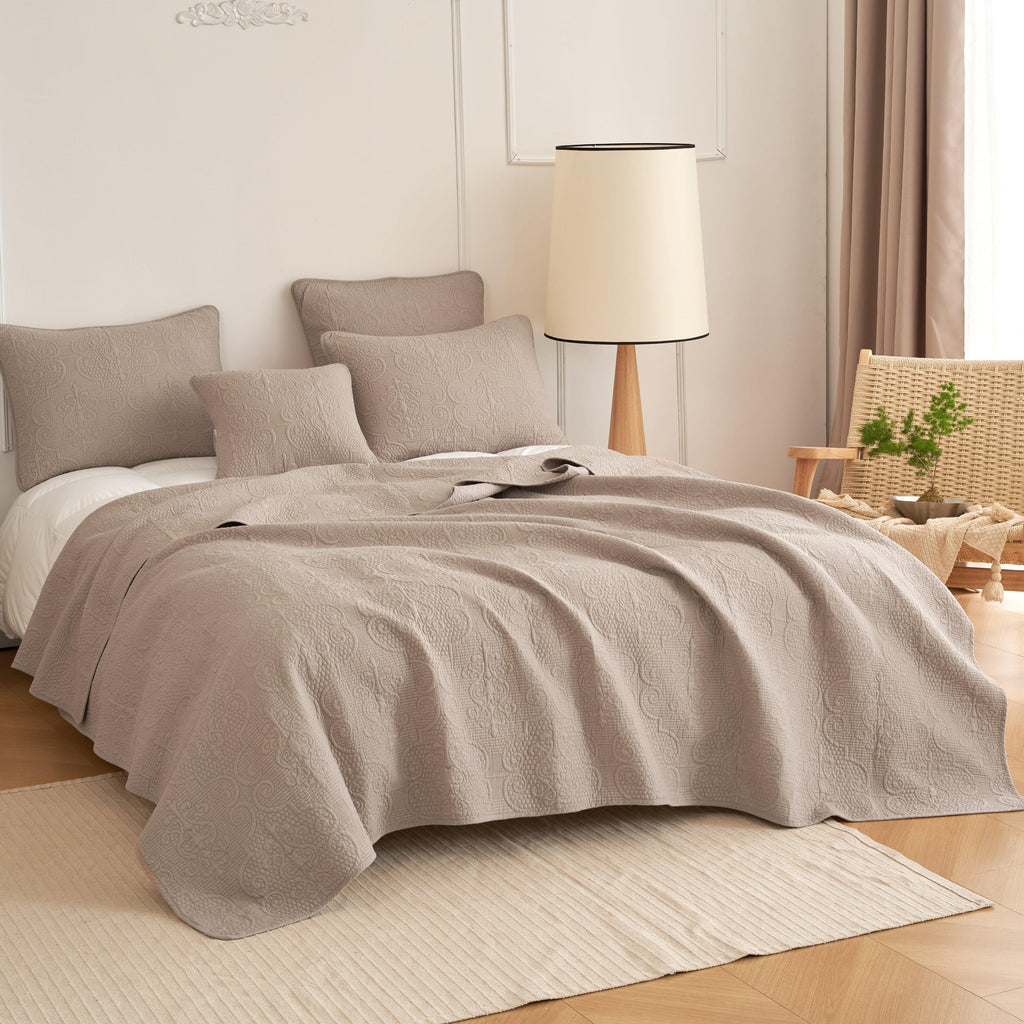 Taupe-beige quilted bedspread set with matching throw pillows on a bed