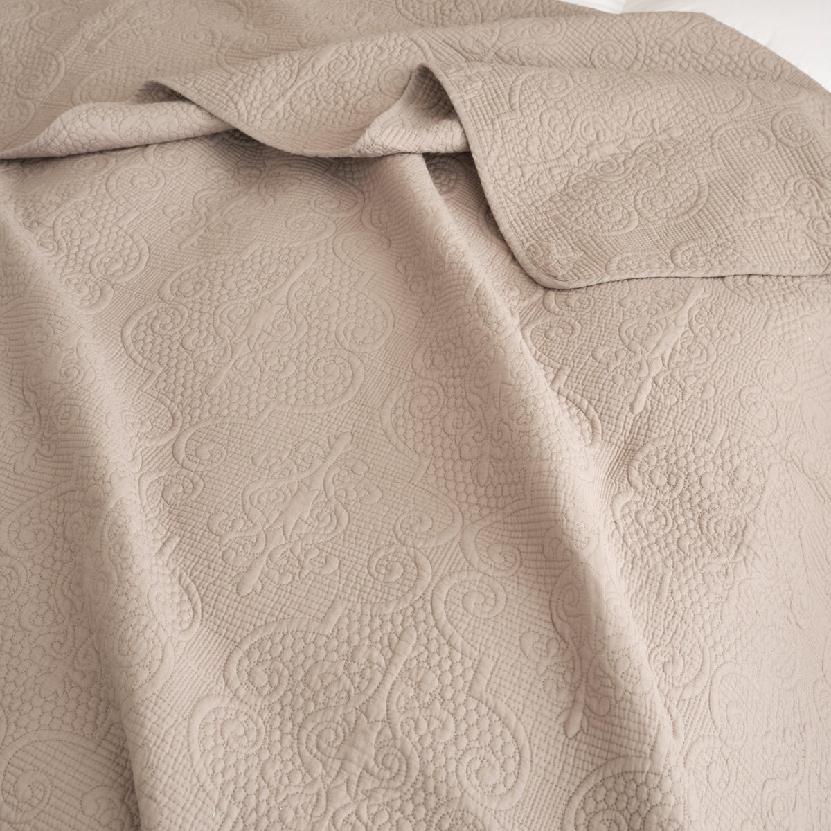 Taupe-beige quilted cotton fabric with raised ornate motifs, folded close-up