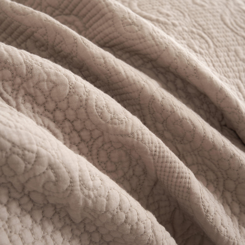 Quilted taupe-beige cotton bedspread with diamond matelasse texture, close-up