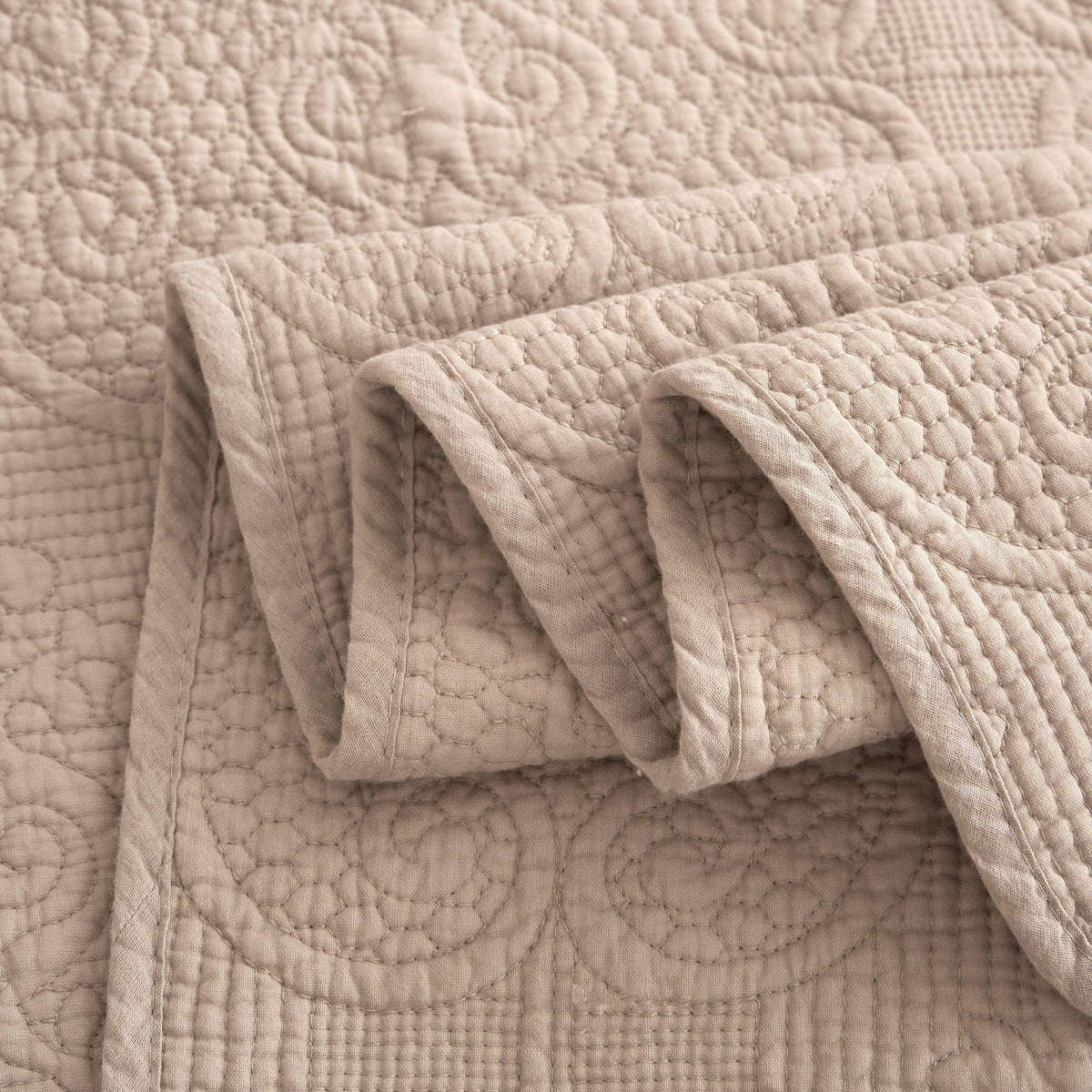 Taupe-beige quilted bedspread with raised diamond stitching, fabric fold detail