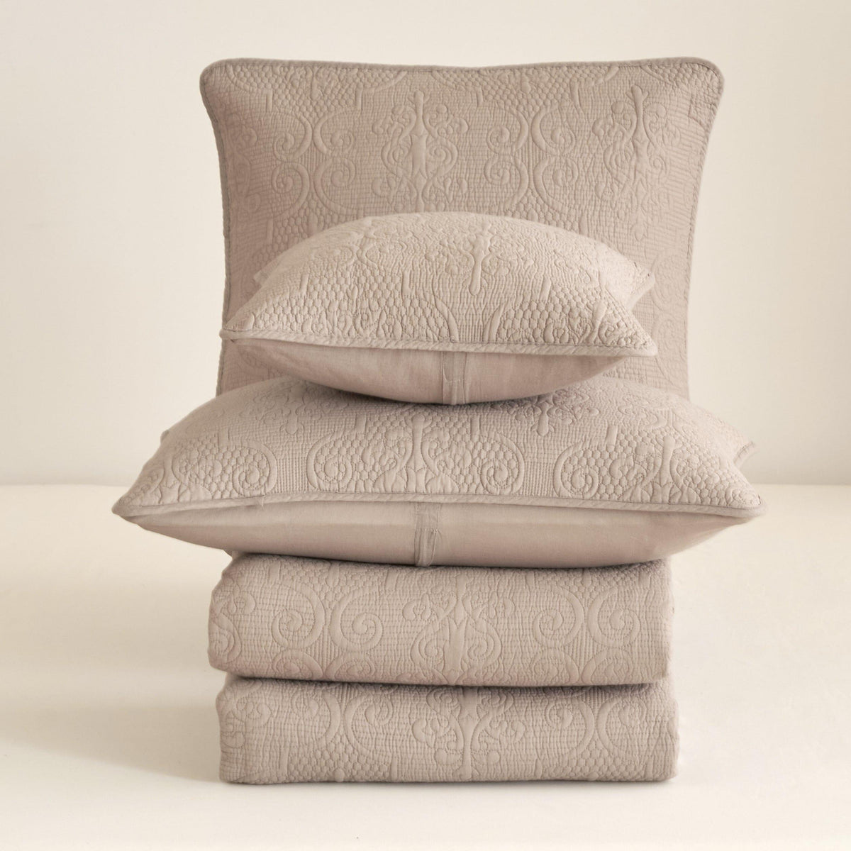 Stacked quilted bedspread and pillows in taupe beige with embossed swirl pattern