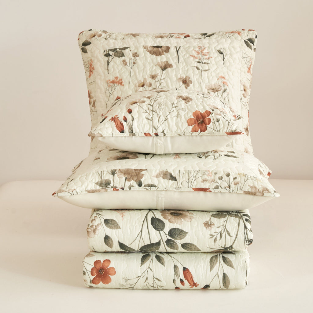 Cream floral quilt set with coordinating pillow shams stacked, quilted texture