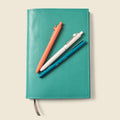 Teal leather refillable notebook cover with stitched edges and gray pull tab strap.