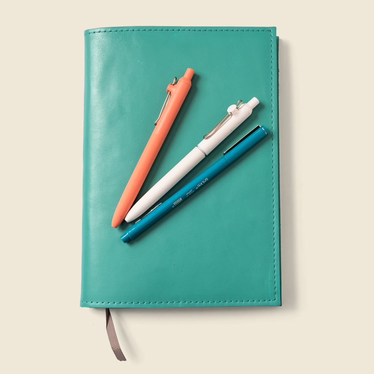Teal leather refillable notebook cover with stitched edges and gray pull tab strap.