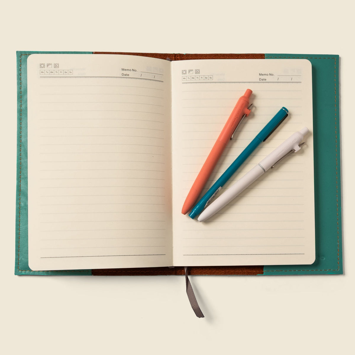 Teal leather notebook cover opened flat with lined pages and pens resting inside.