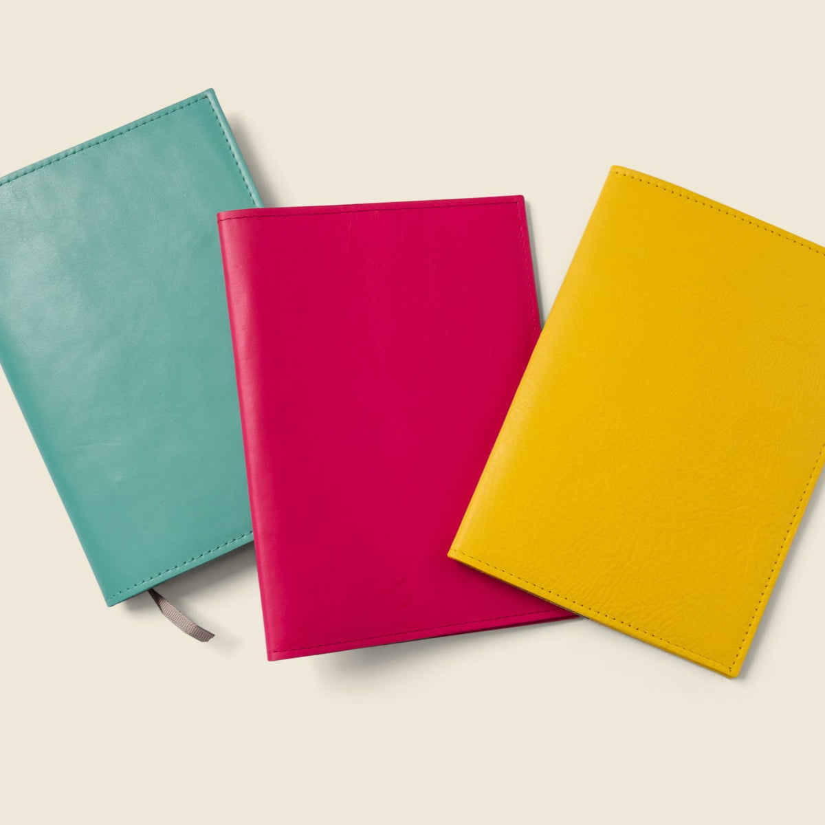 Leather notebook covers in teal, magenta, and yellow with gray pull tab straps.