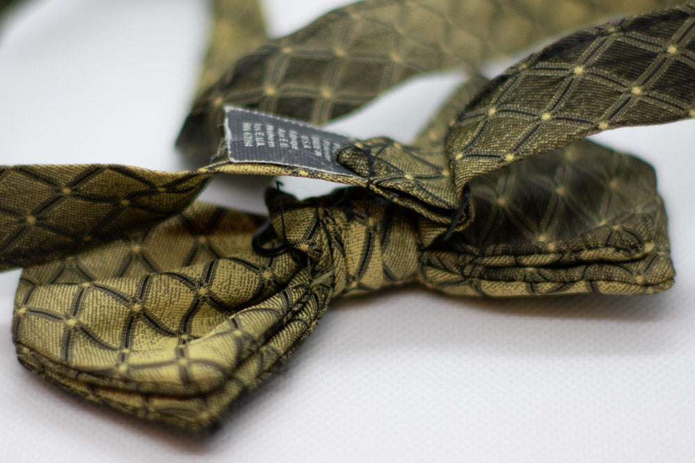 Adjustable bow tie in dark olive and gold geometric pattern with adjustable strap and label
