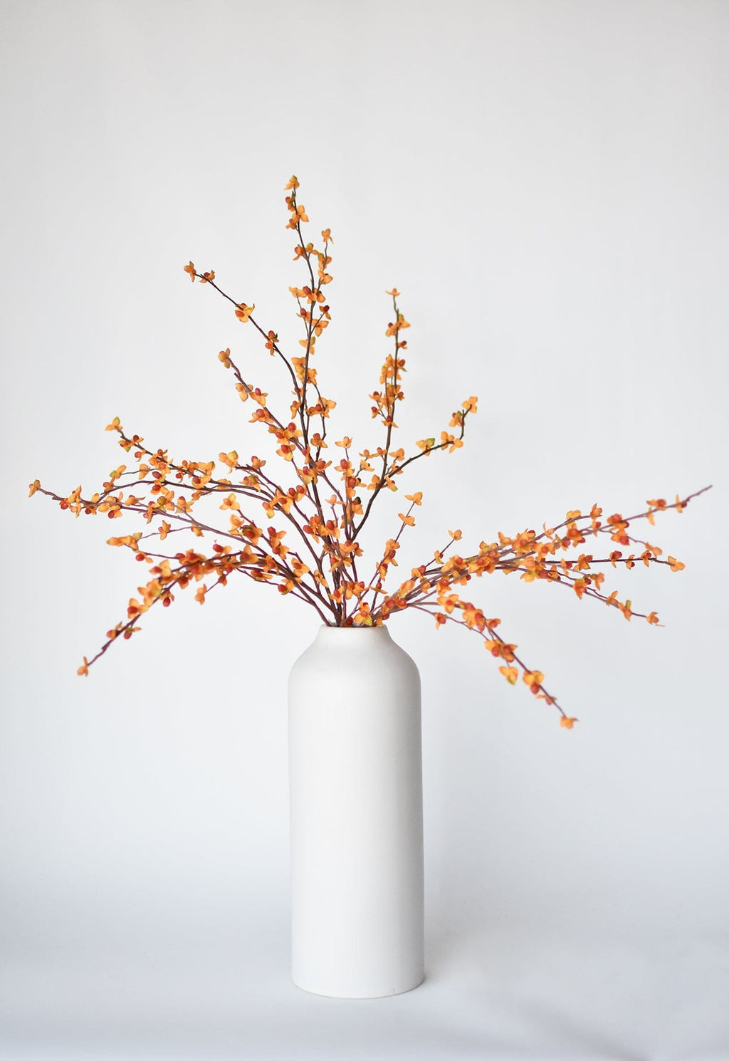Faux bittersweet stem with orange and yellow berry clusters, shown in white vase
