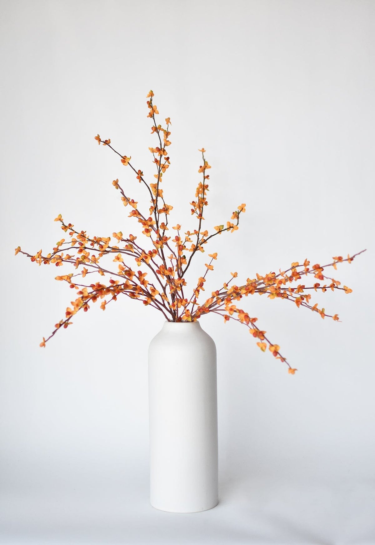 Faux bittersweet stem with orange and yellow berry clusters, shown in white vase