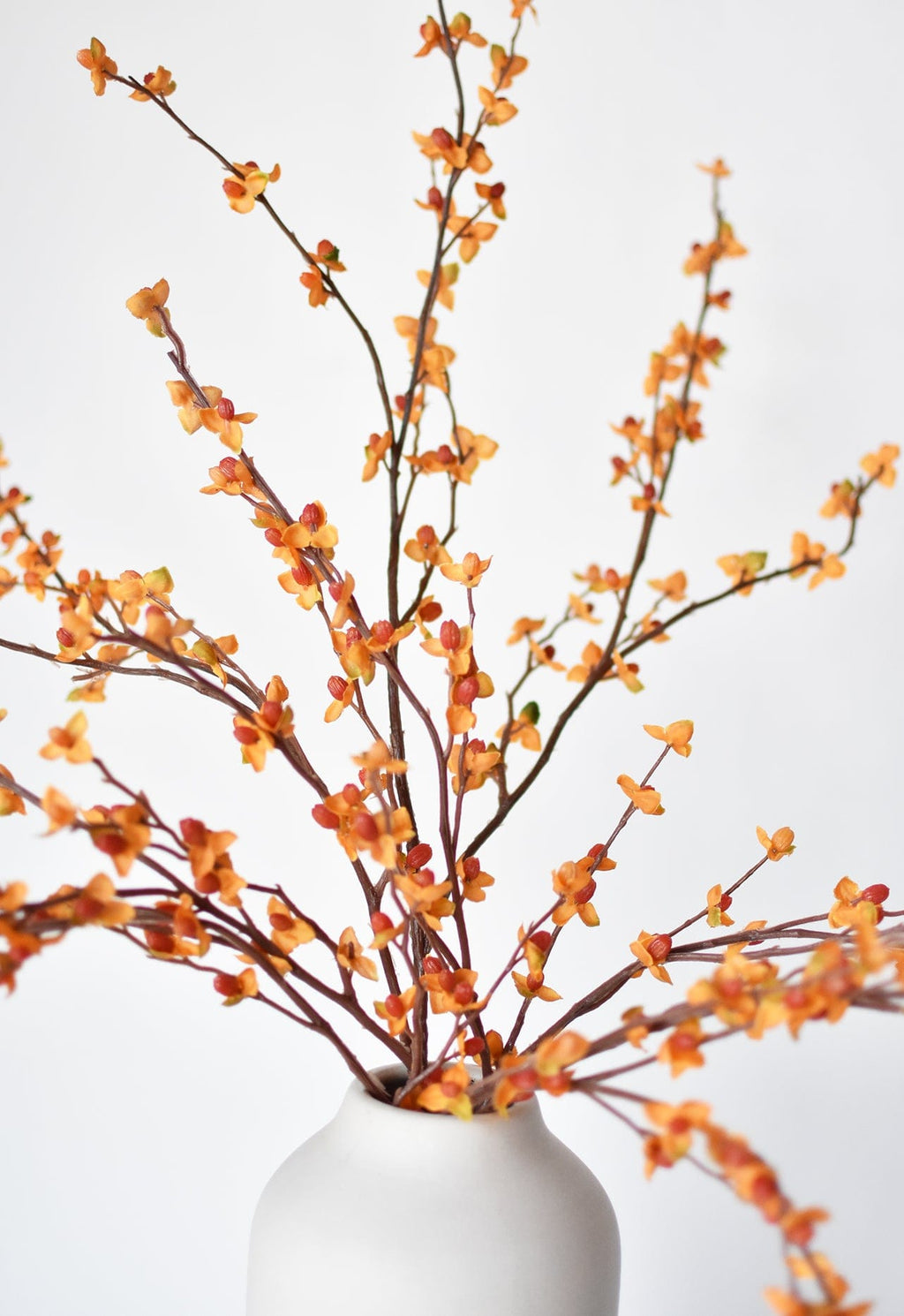 Faux bittersweet stem with orange and yellow berry clusters, in white vase