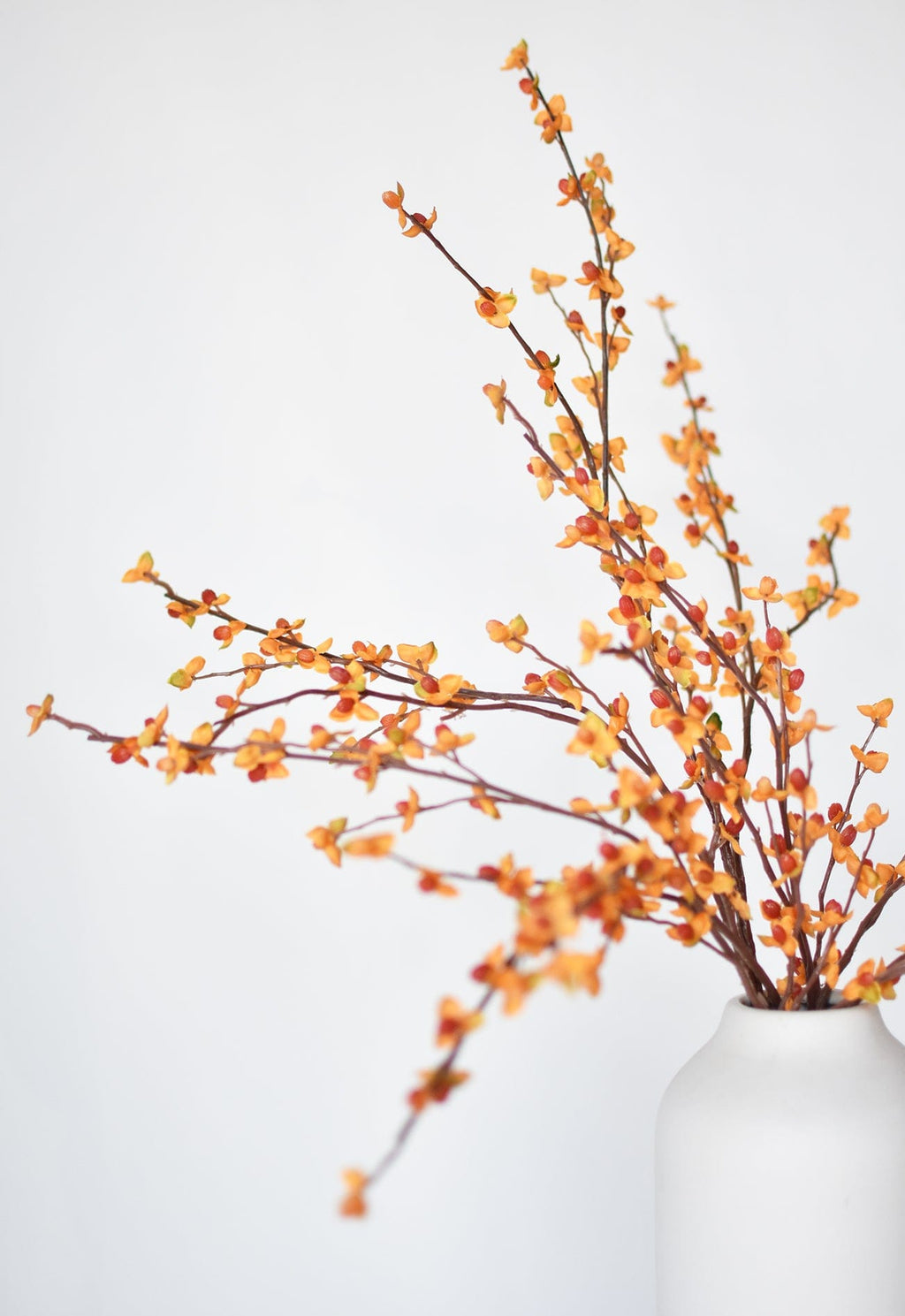 Faux bittersweet stem with orange and yellow berry clusters, partially in white vase