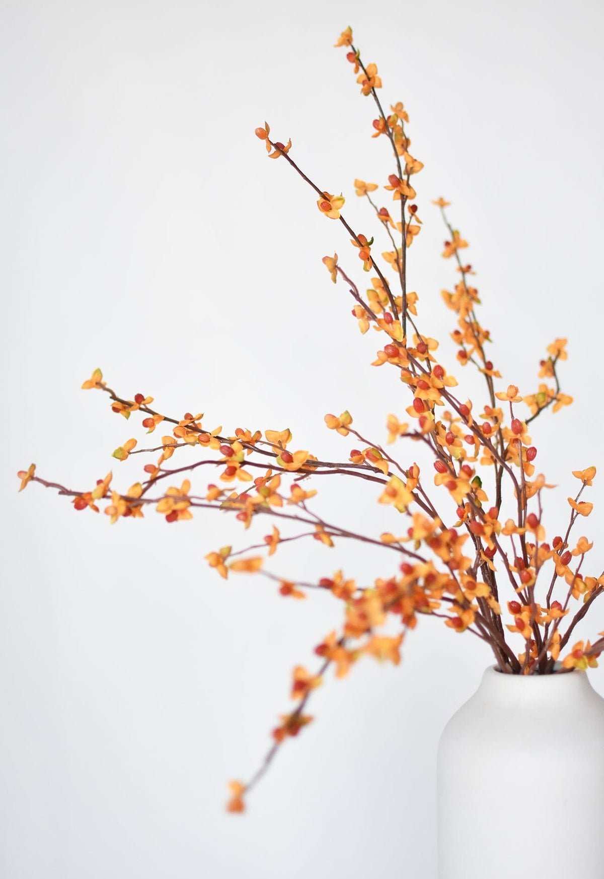 Faux bittersweet stem with orange and yellow berry clusters, partially in white vase
