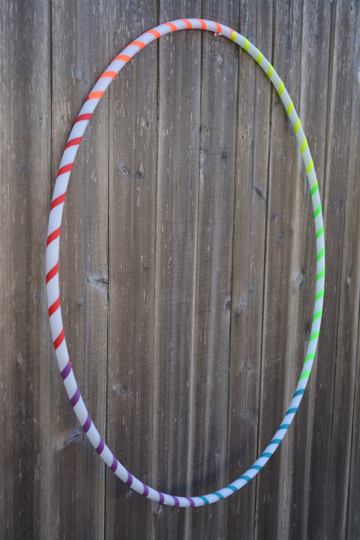 Beginner hula hoop with multicolor spiral gaffer tape against wooden fence