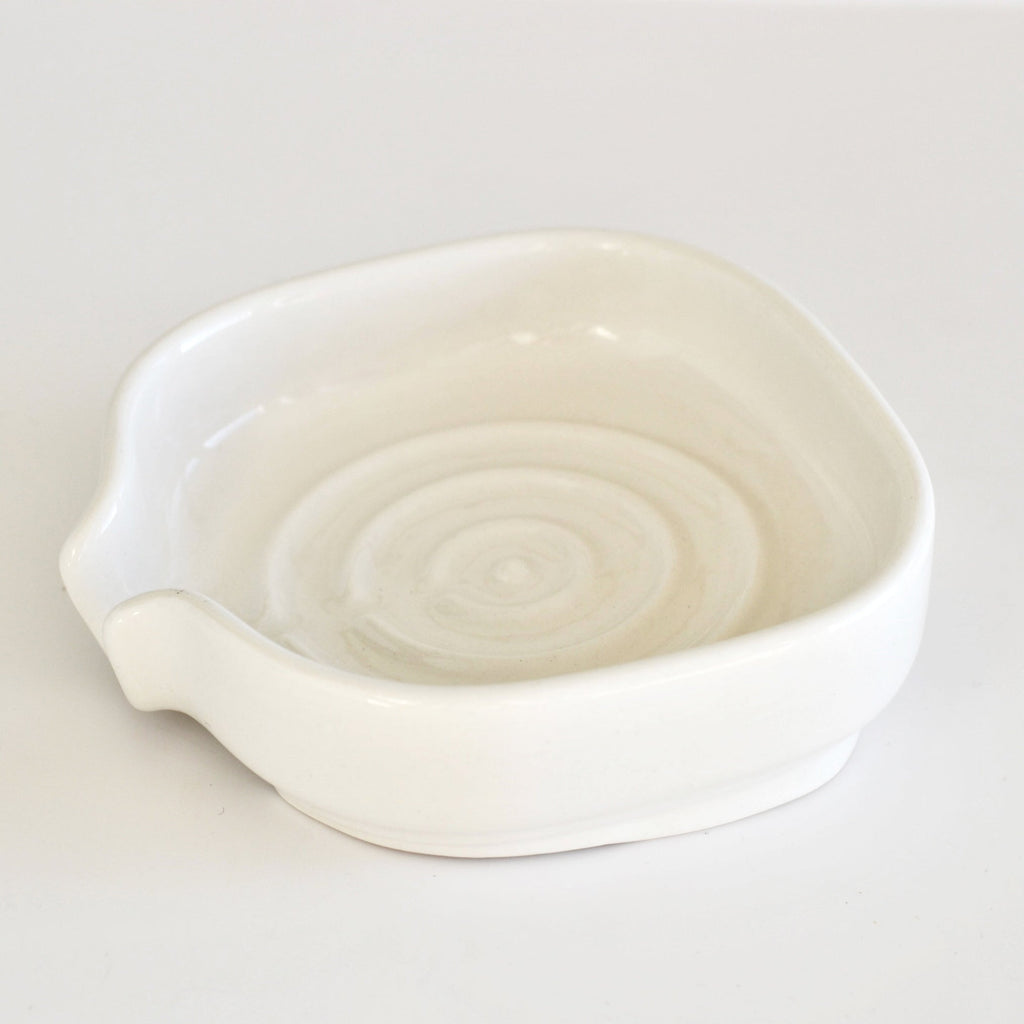 White glossy porcelain soap dish with shallow bowl, front spout, and drain base