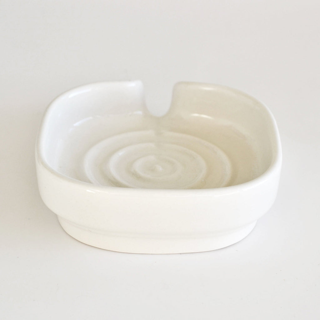 White glossy porcelain soap dish with two side grips and swirl drain channel